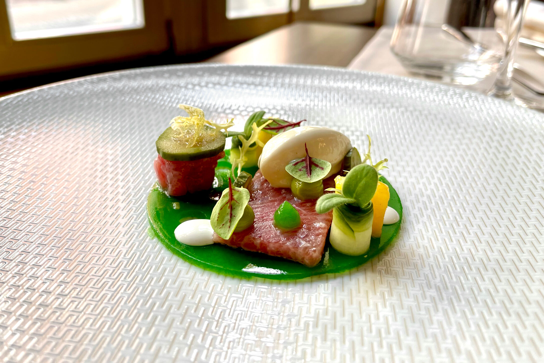 Balfego-Thunfisch auf Glasteller, in feinen Scheiben auf grünem Soßenspiegel angerichtet.