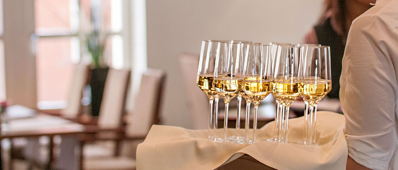 Weibliches Serviceteam im „Engels in der Burg“ serviert Champagner, eleganter Raum im Hintergrund.