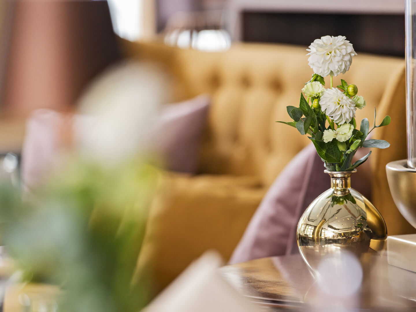 Blumen in goldener Vase vor gelbem Samtsofa im stilvollen Restaurant Engels.