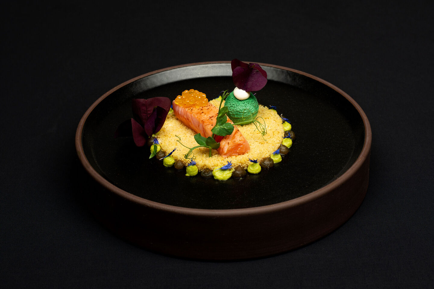 Label Rouge Lachs mit Erbse, kunstvoll auf schwarzem Teller angerichtet.