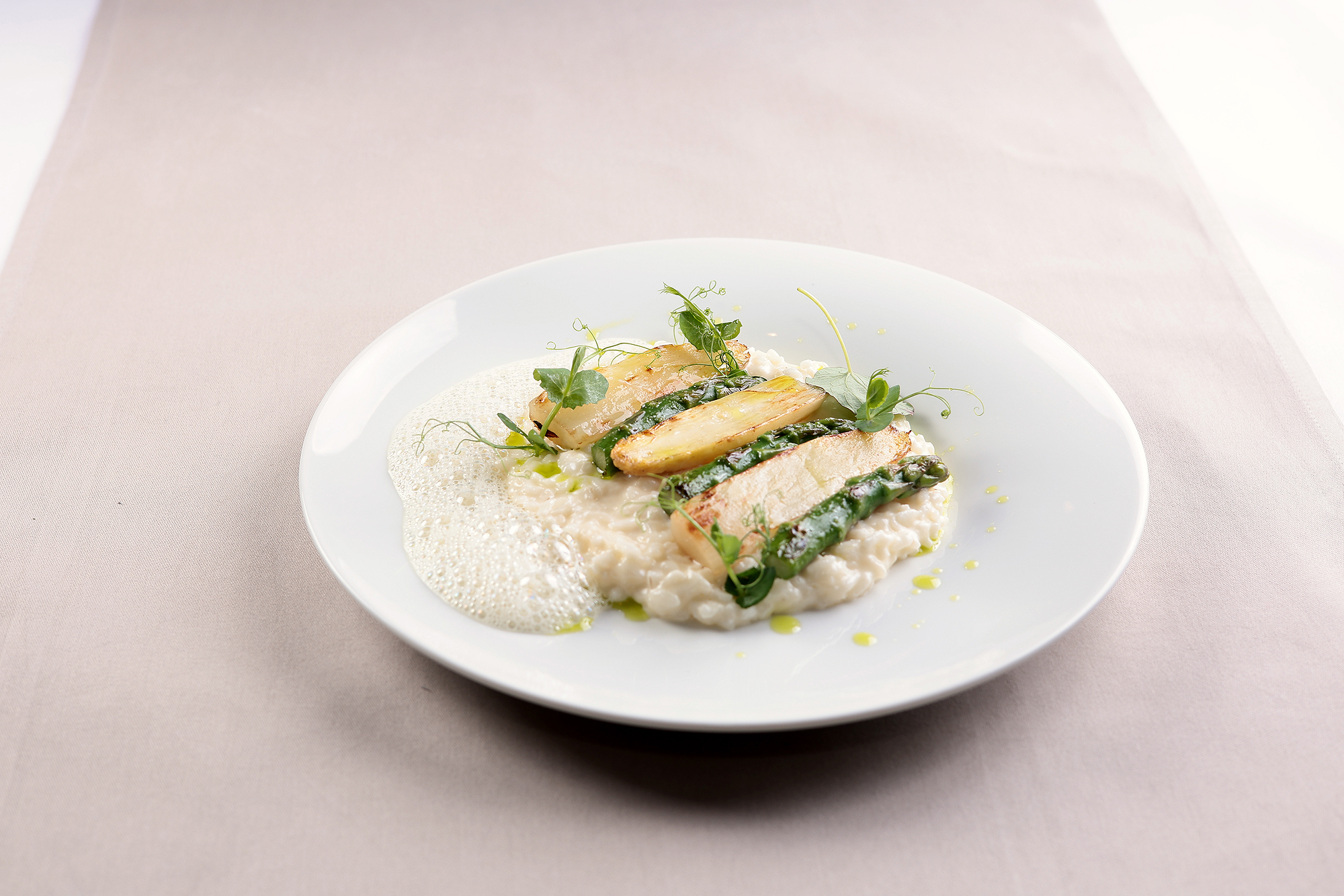 Spargelrisotto in grünen und weißen Tönen, garniert mit weißem Schaum, elegant abgerundet.