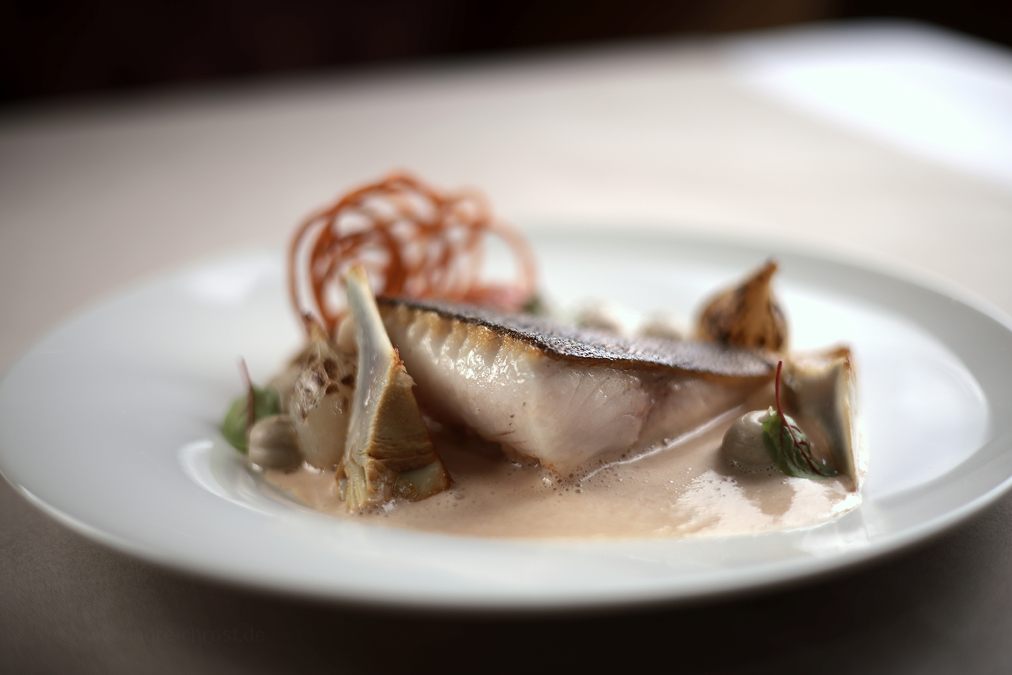 Zartes Stück Black Cod auf weißem Teller, im sanften Bokeh elegant präsentiert.