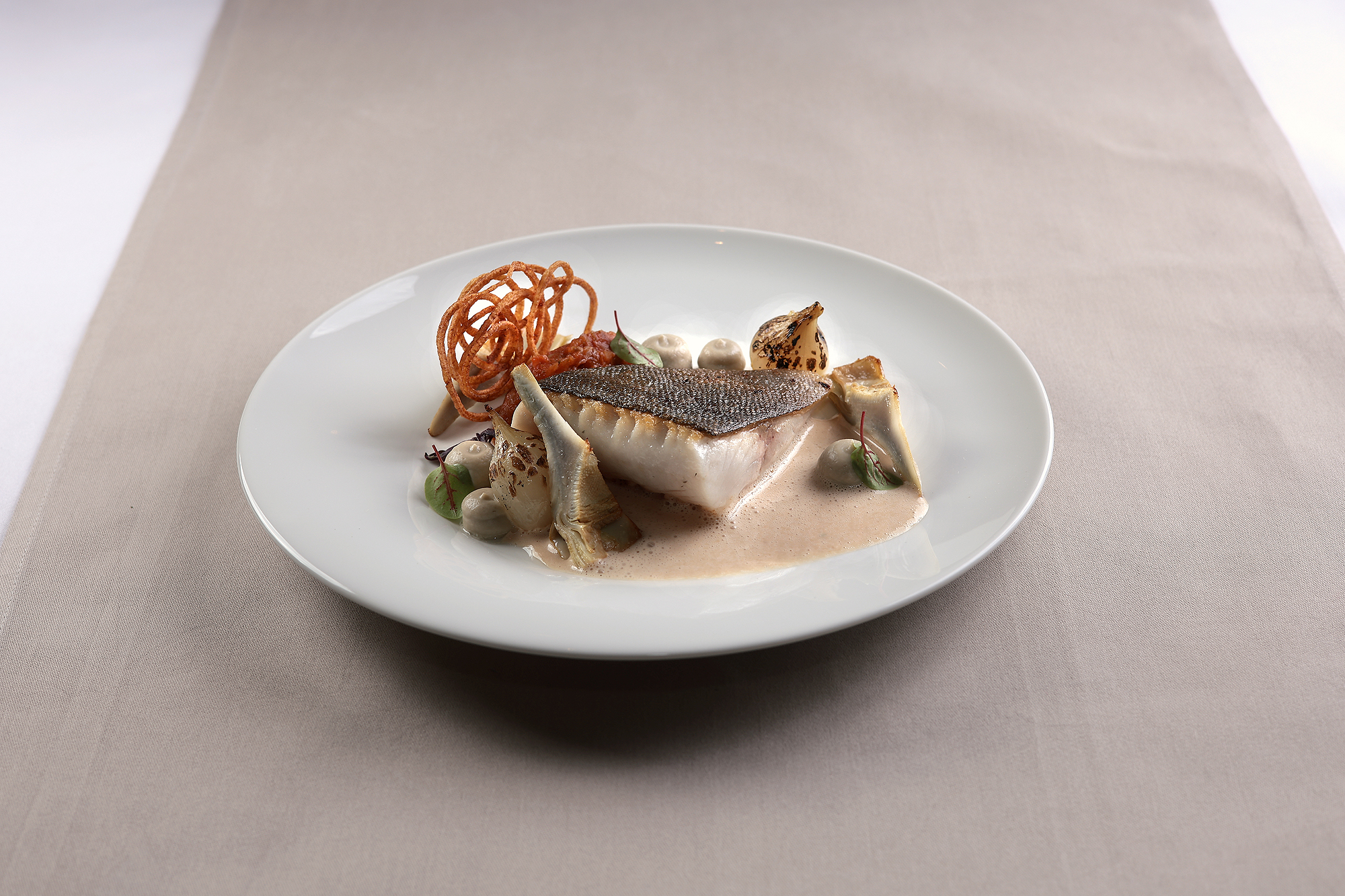 Elegantes Fine-Dining-Gericht mit Black Cod, Artischocken und frischen Tomaten.