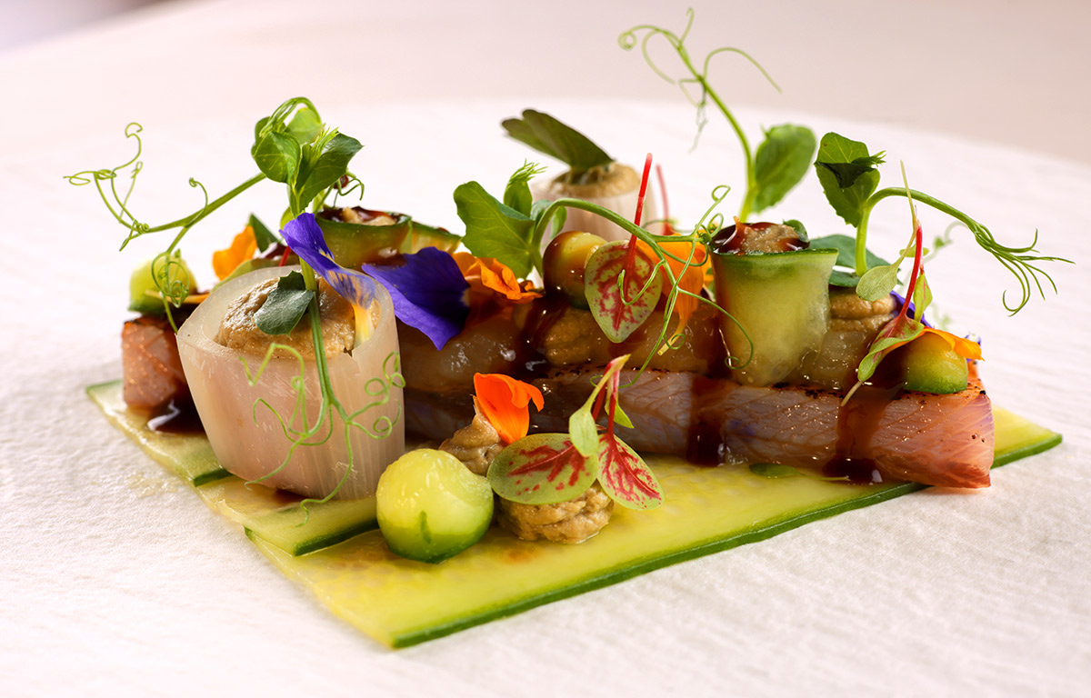 Fischfilet auf Zucchinischeiben, dekoriert mit Sauce, Kräutern und essbaren Blüten.