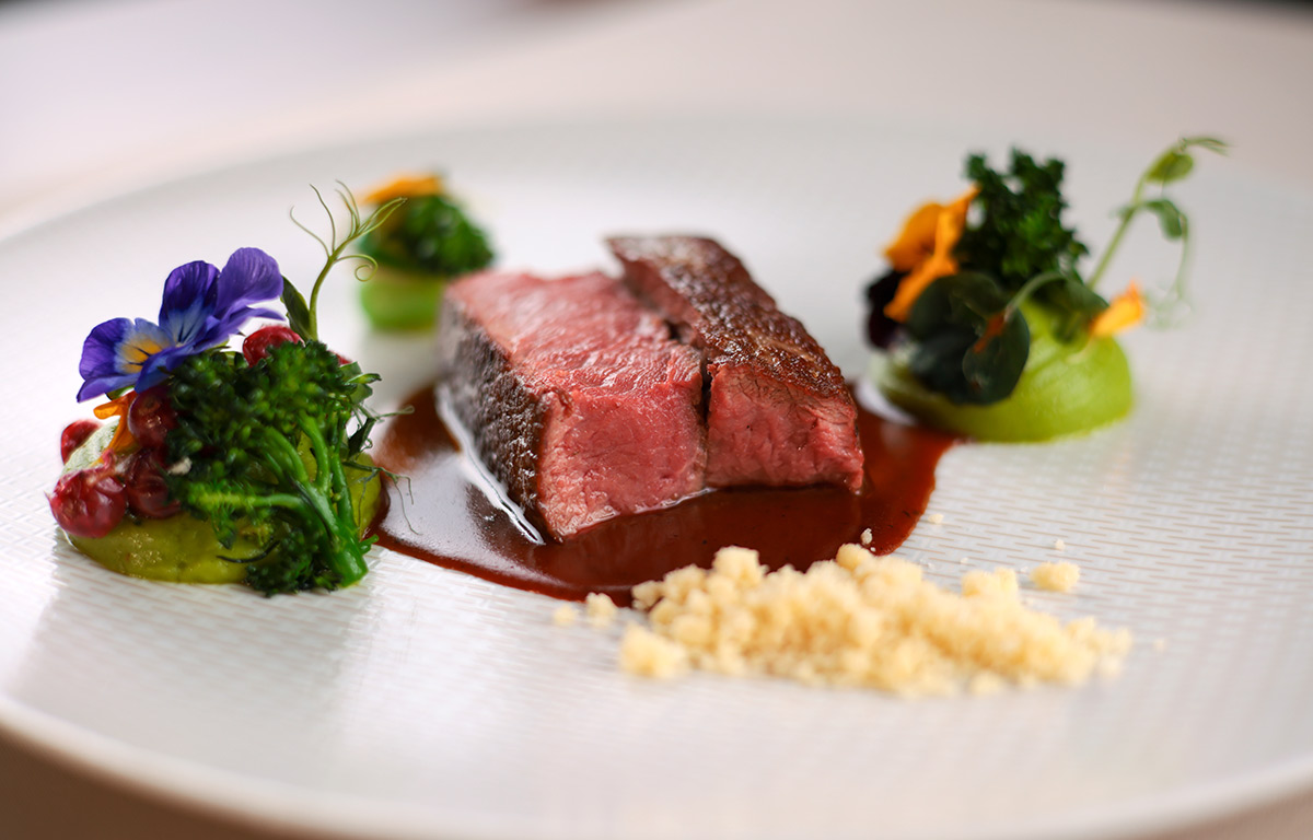 Elegant angerichtetes Salzwiesenlamm mit Spinatpüree, Preiselbeeren und Brokkoli.