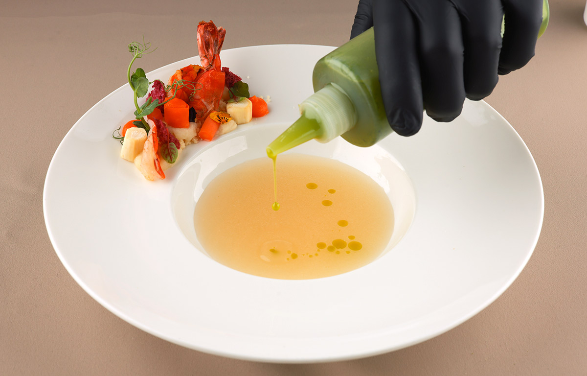 Pastinaken-Essenz mit Kräuteröl, Garnele am Tellerrand, elegant verfeinert.