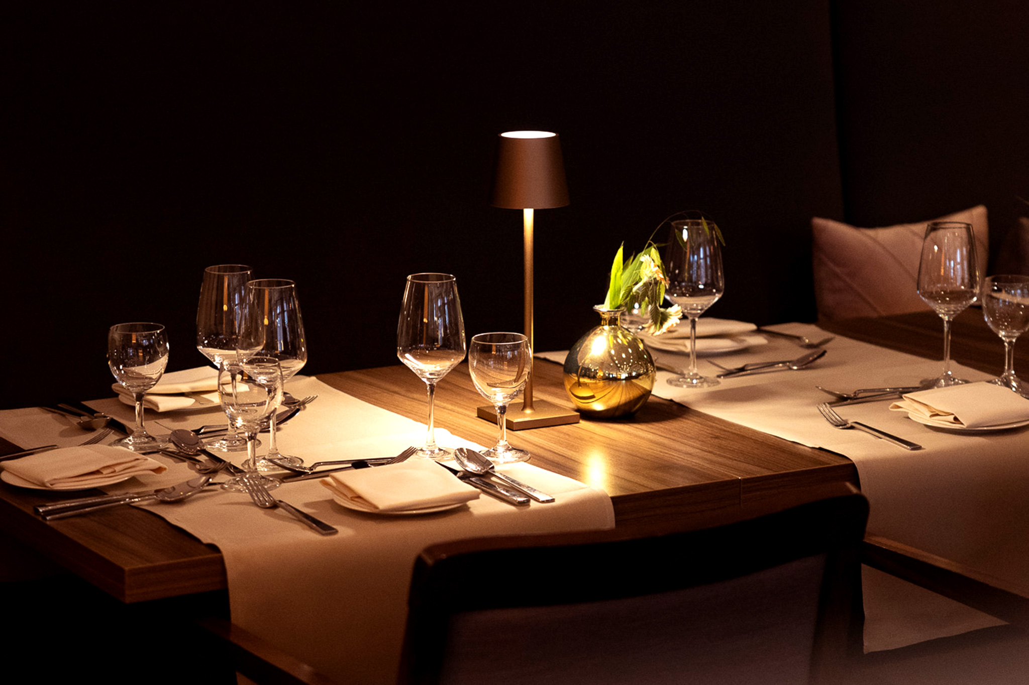Gedeckter Tisch in warmer Atmosphäre, leere Gläser warten auf Füllung, gemütlich beleuchtet.