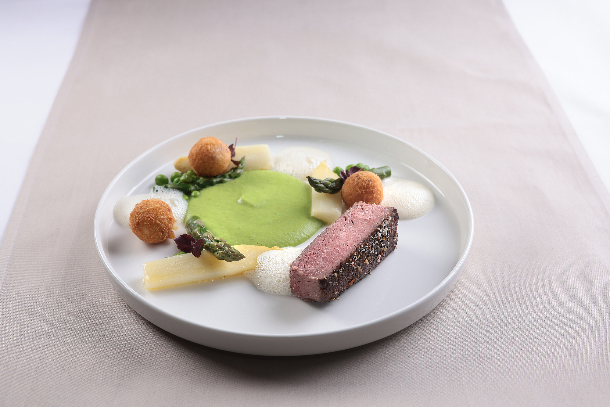 Zarter US-Rindertafelspitz, serviert mit frischem Spargel und Erbsen.